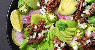 Instant Pot carnitas in a bowl with lettuce, limes, avocados, and jalapenos.