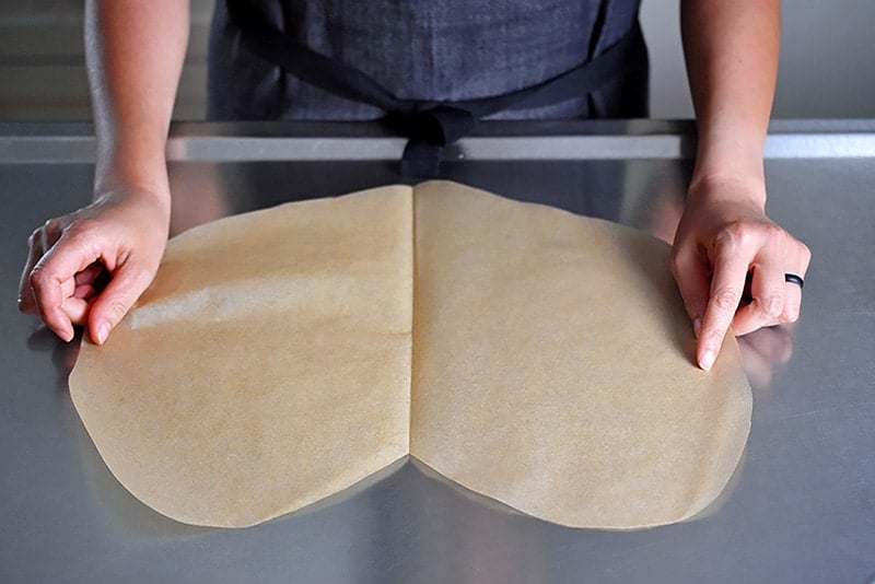 Someone laying flat the heart-shaped parchment paper on a countertop for the paper-wrapped chicken recipe.