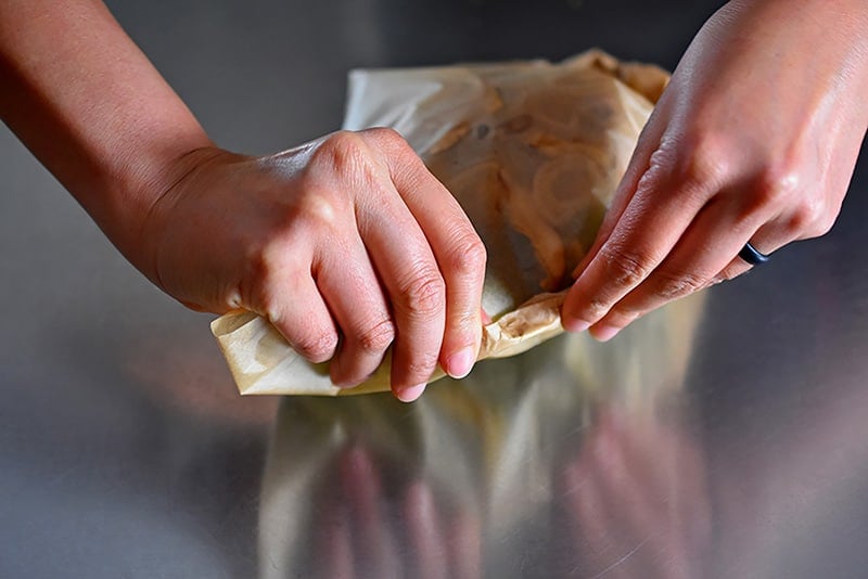 Someone crimping the edges of the parchment paper with the ingredients inside for the paper-wrapped chicken recipe.
