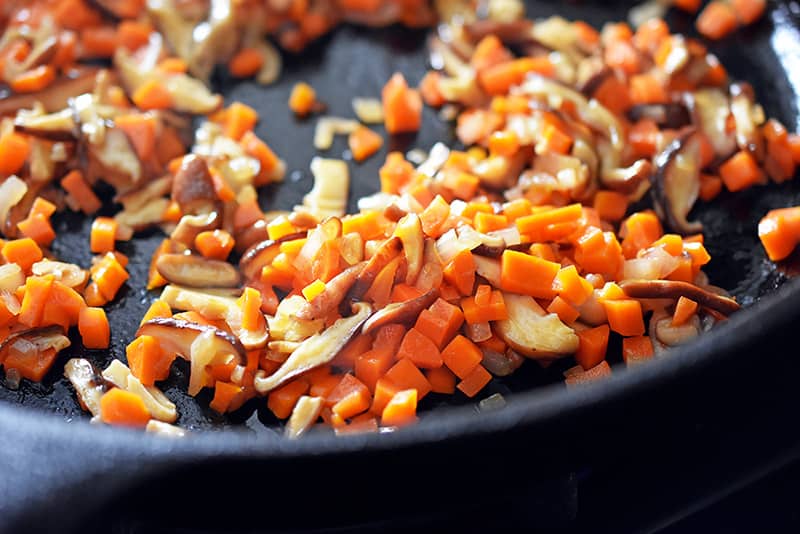 Sautéing the carrots, shallots, and shiitake mushrooms in a cast iron skillet until softened.
