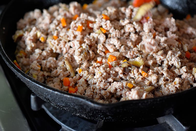 A closeup of ground pork and veggies in a cast iron skillet for egg roll in a bowl.
