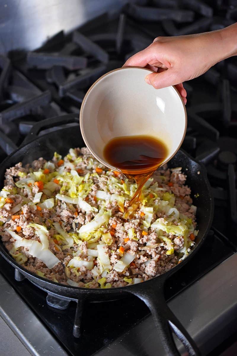 Pouring the sauce into a skillet filled with egg roll in a bowl. 