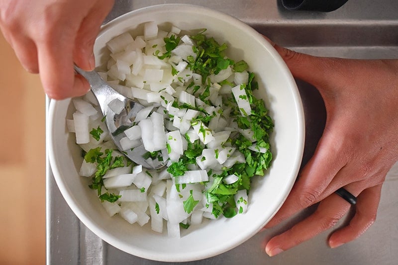 Someone stirring in a small bowl diced onions with chopped cilantro.
