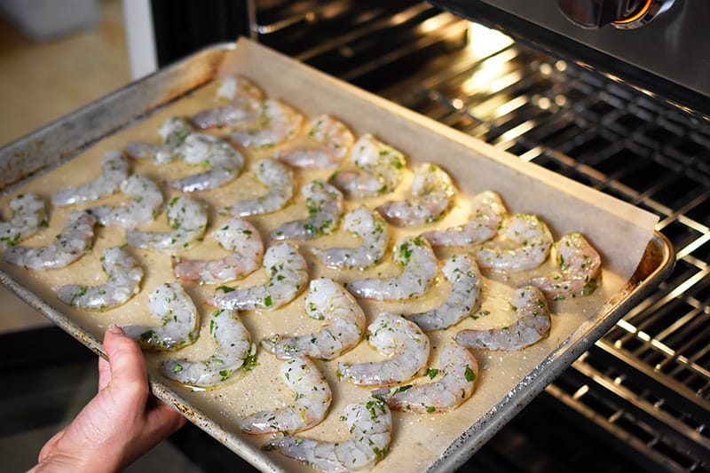 Someone placing the paleo shrimp on a baking sheet into the oven.