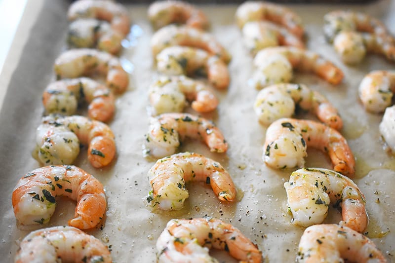 Paleo shrimp roasted in the oven on a parchment-lined baking sheet, lightly cooked and slightly pink.