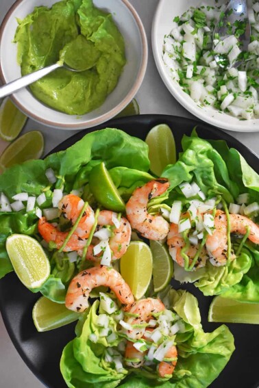 An overhead shot of Paleo Shrimp Tacos on a bed of lettuce. There is a bowl of Avocado Crema on the top left.