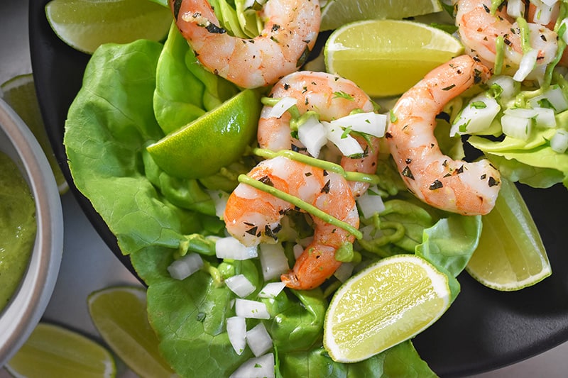 An overhead shot of paleo shrimp tacos on butter lettuce with cilantro, onions, and lime.