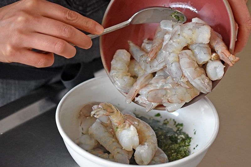 Someone is adding raw shrimp to a bowl of marinade to make paleo, Whole30, and keto shrimp tacos.