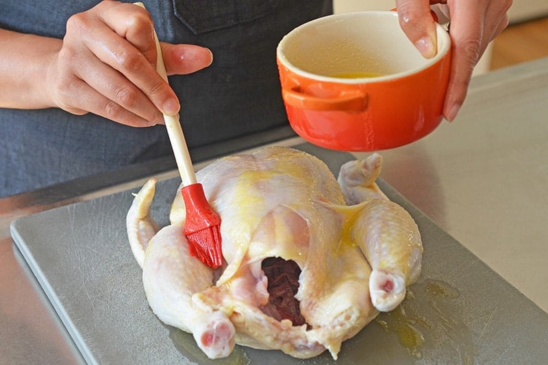 Brushing melted ghee on a raw whole chicken on a gray cutting board to make healthy weeknight roast chicken