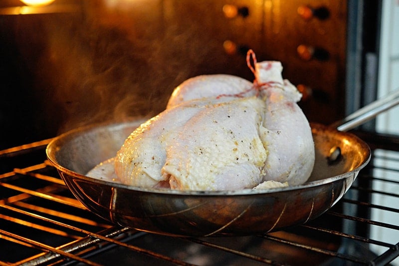 A raw whole chicken is placed breast-side up in a hot skillet in the oven 