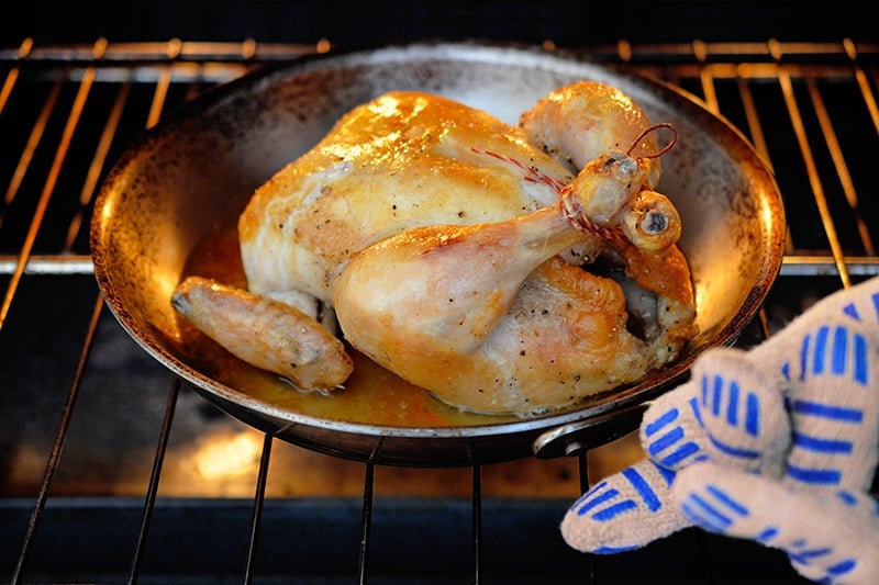 Removing a healthy and easy Weeknight Roast Chicken in a skillet from the oven.