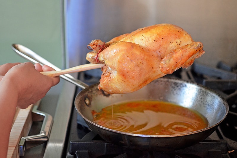 Using a spatula to drip juices from Weeknight Roast Chicken into a skillet.