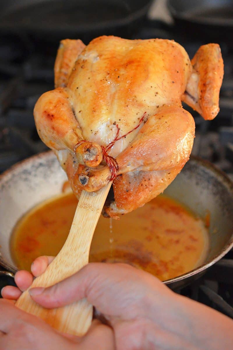 The handle of a wooden spatula is used to help the juices from Weeknight Roast Chicken flow into a frying pan.