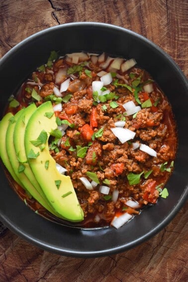 Whole30 Instant Pot ground beef chili in a bowl topped with onions and avocado.