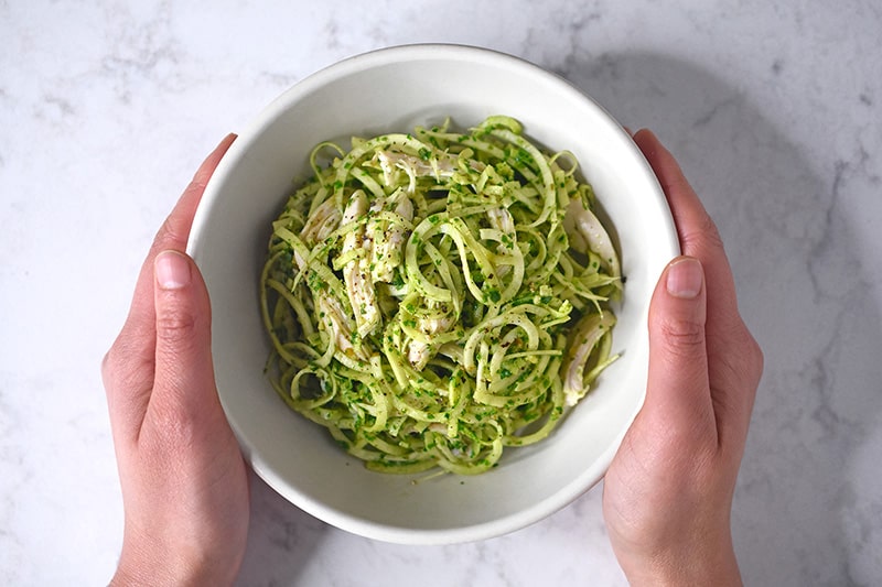 Someone holding onto a bowl of zoodles with arugula pesto with both hands.