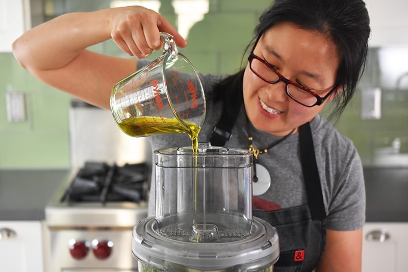 Someone pouring in a stream of olive oil into a food processor.