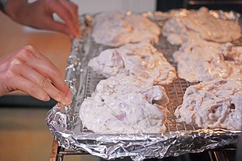 A tray of Umami Roast Chicken is being placed in the oven with the skin side down.
