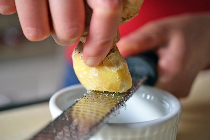 Someone grating frozen ginger on a microplane into a small ramekin.