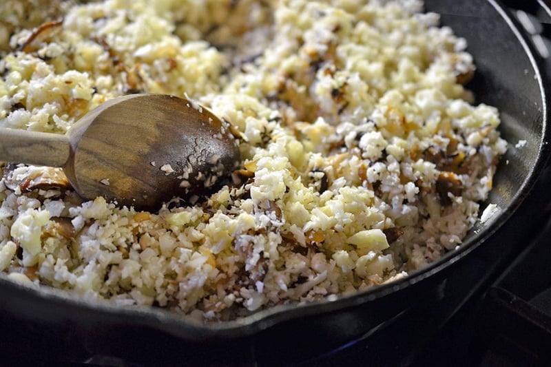 Adding the cauliflower rice to the skillet.