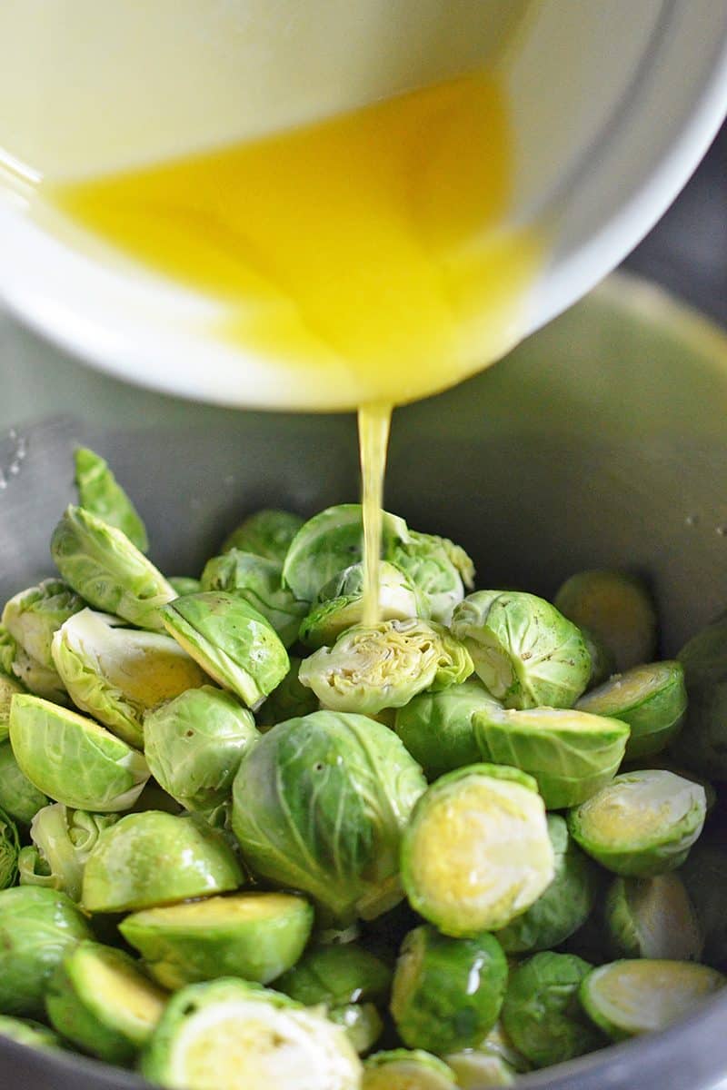 Melted ghee is poured into a bowl containing halved Brussels sprouts