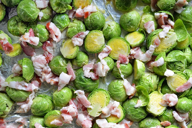 An overhead shot that shows Roasted Brussels sprouts and bacon in a tray ready for the oven.