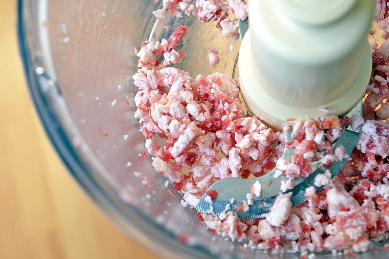 Frozen bacon getting pulsed in a food processor.