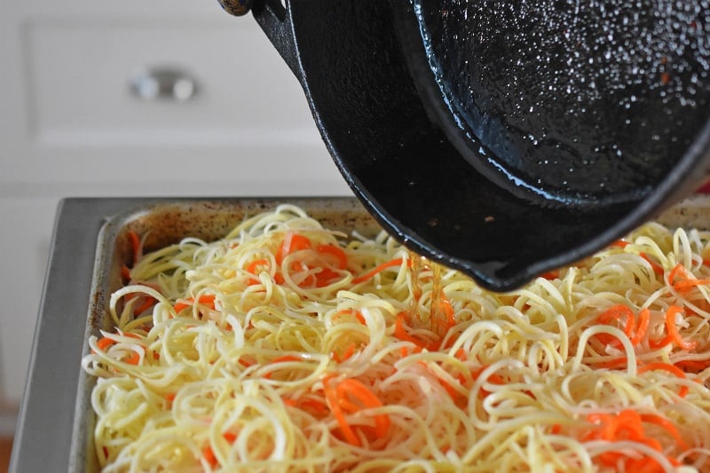The reserved bacon grease is poured onto the salted spiralized vegetables.