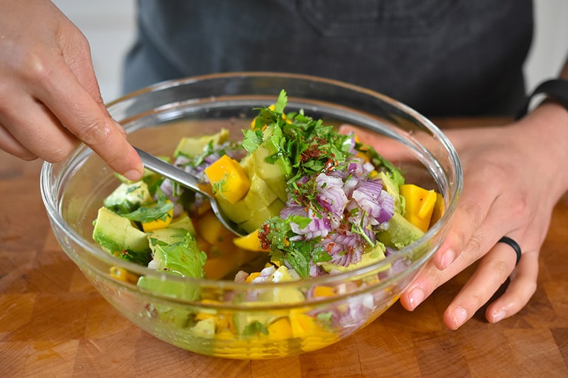 Tossing the ingredients of avocado, mango, red onion, cilantro, olive oil, salt, and red pepper flakes.