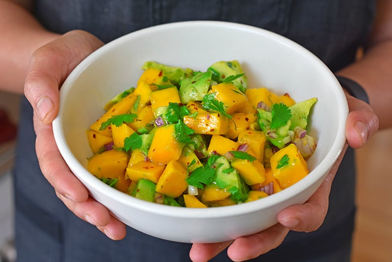 Someone presenting a bowl of the paleo and Whole30 mango and avocado salsa.