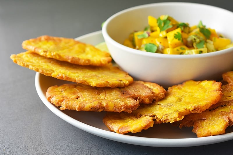 Close up of a plate of fried green plantains with a bowl of the paleo and whole30 mango avocado salsa.
