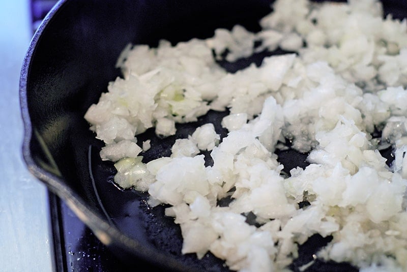 Minced onions sautéing in a large cast iron skillet.