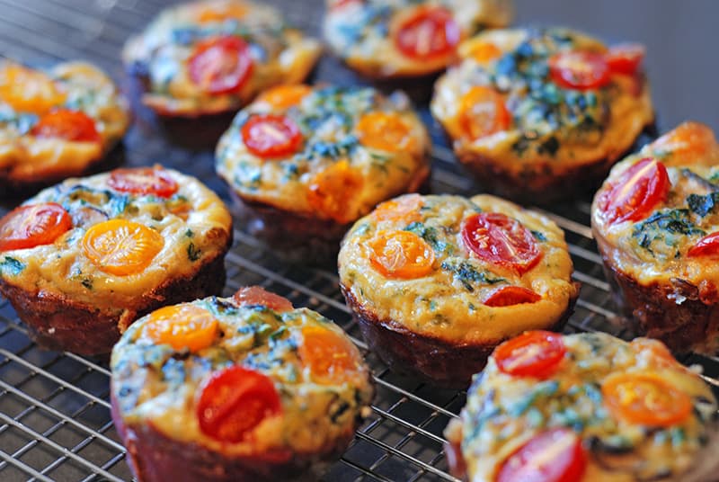 A bunch of Prosciutto-Wrapped Mini Frittata Egg Muffins cooling on a wire rack.
