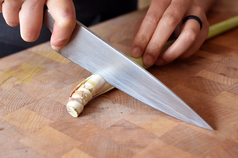 Cutting the tough end off of a lemongrass stalk on a wooden cutting board.