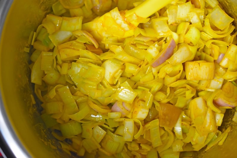 An overhead shot inside an Instant Pot of sautéed leeks and curry seasoning