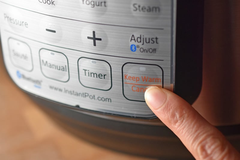 A finger pressing the Keep Warm / Cancel button on an Instant Pot.