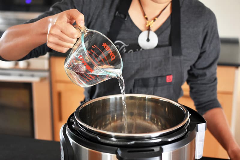 Someone is pictured pouring one cup of water into an Instant Pot.
