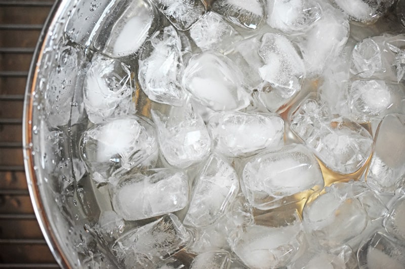 An overhead shot of a stainless steel mixing bowl filled with ice and water.