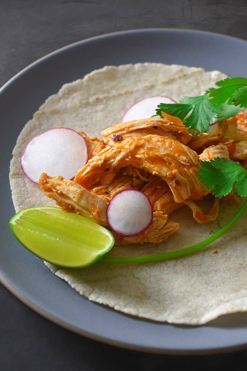 A plate of Instant Pot Salsa Chicken Tacos on a grain-free tortillas and garnished with lime, radishes, and cilantro.