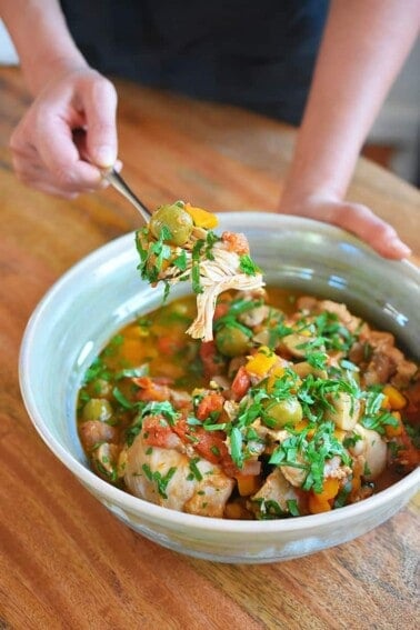 Someone spooning out Instant Pot Summer Italian Chicken out of a light blue serving bowl.