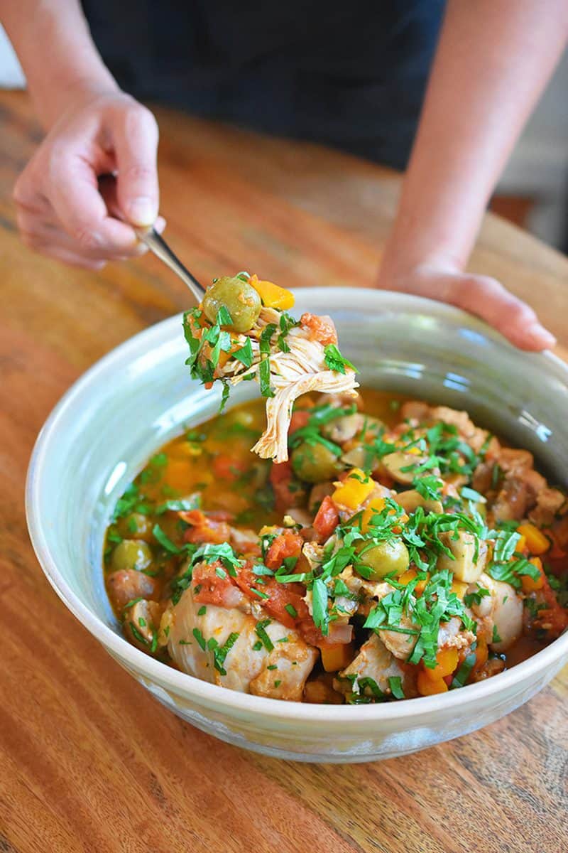 A hand is spooning Whole30, keto, Paleo Instant Pot Summer Italian Chicken out of a serving bowl.