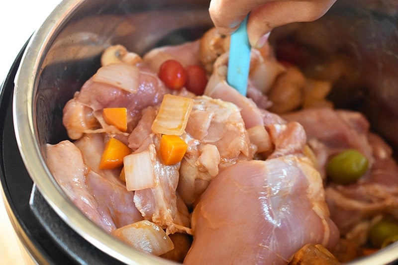 A person is stirring the raw ingredients for the Instant Pot Summer Italian Chicken stew before putting on the lid.