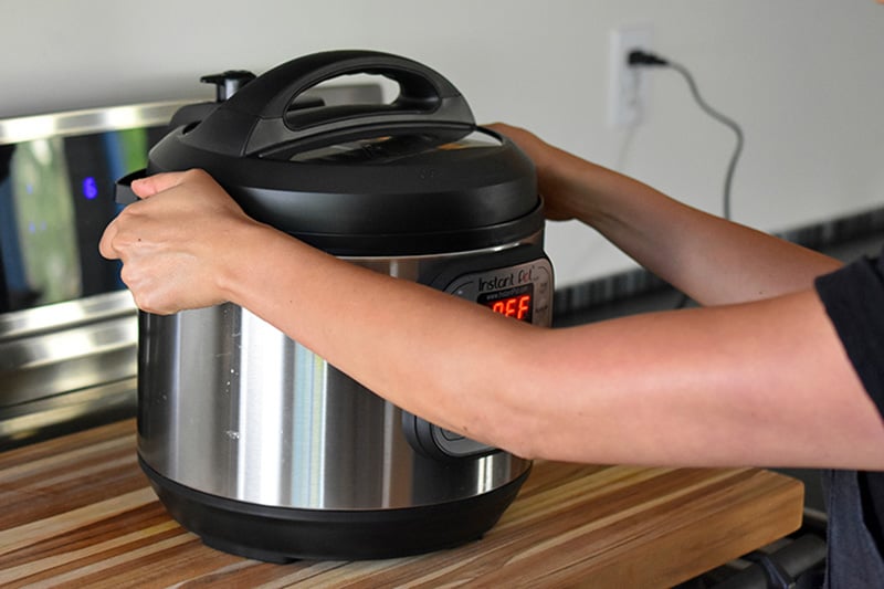 A person is putting an Instant Pot filled with Summer Italian Chicken stew under a vent.