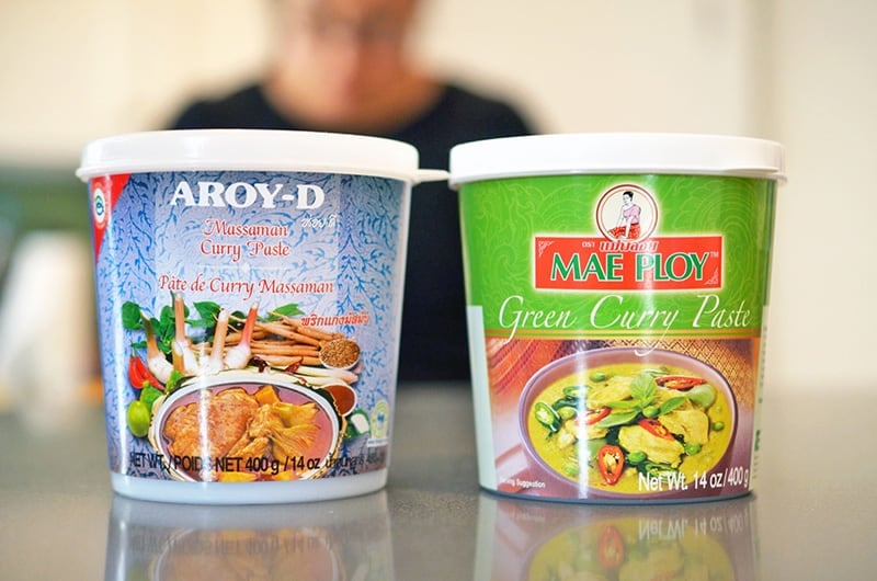 Two containers of Thai curry pastes on the counter, Aroy-D's Massaman Curry Paste and Mae Ploy's Green Curry Paste.