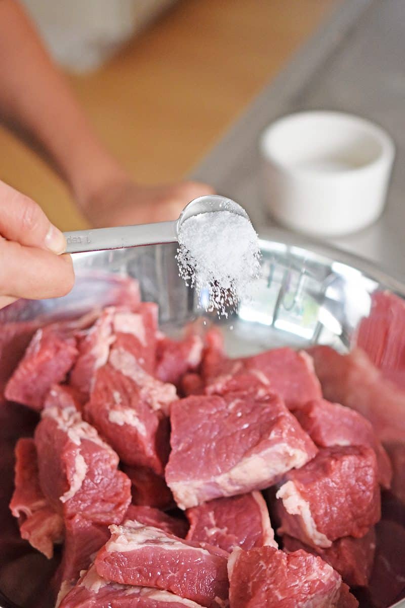 Salt is sprinkled on cubed beef in a silver bowl. 