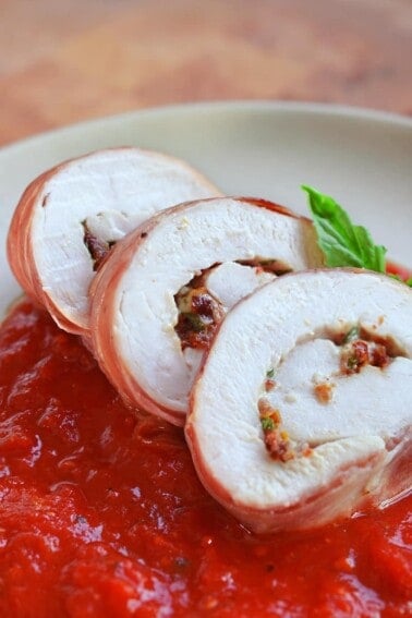 Sliced Chicken Prosciutto Involtini is resting on an angle on a bed of marinara sauce.