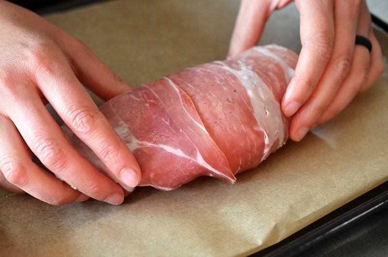 Prosciutto is wrapped around the chicken packets and placed on a parchment lined baking sheet.