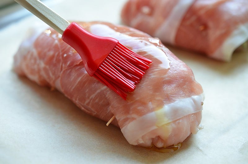 Brushing olive oil on top of Chicken Prosciutto Involtini with a red silicone brush.