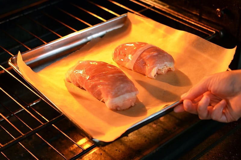 Two Chicken Prosciutto Involtini on a parchment lined baking sheet are placed in the oven.