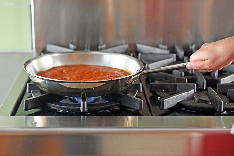 A side view of marinara sauce heating up in stainless steel skillet.