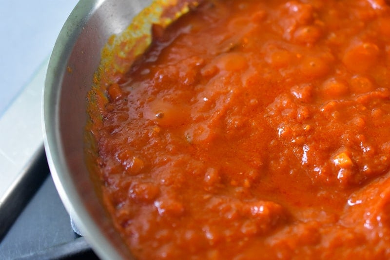 A closeup of marinara sauce bubbling in a stainless steel skillet.